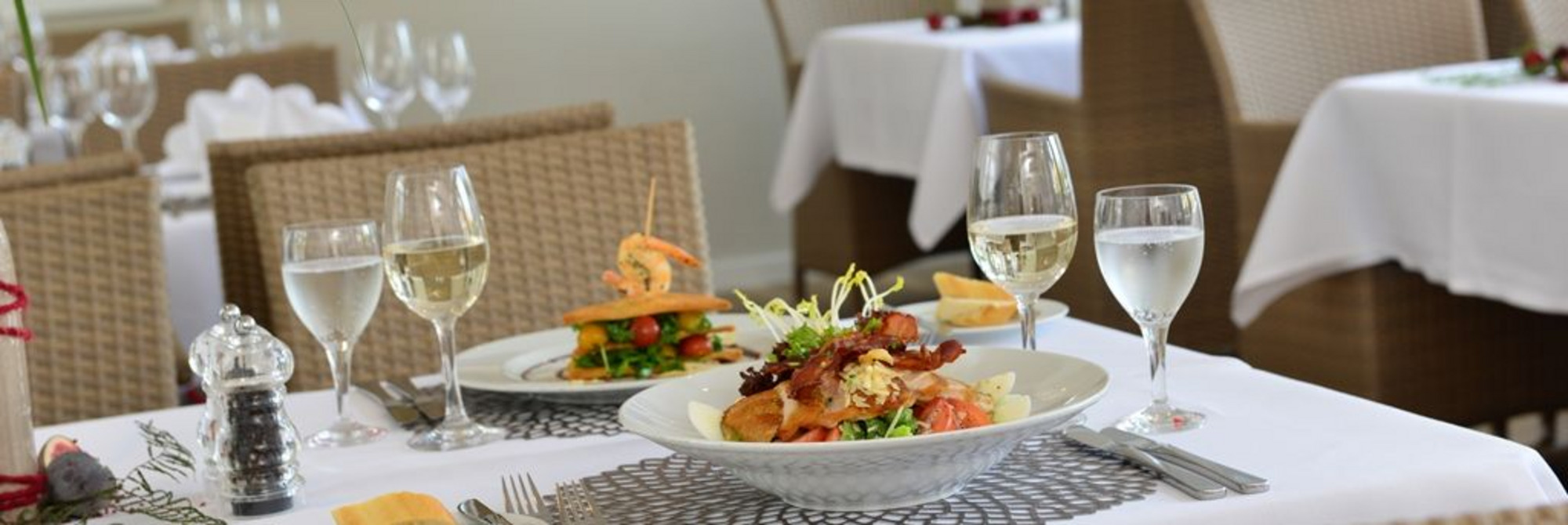 Weiß eingedeckter Tisch mit Fleischgericht, Gemüse, Meeresfrüchten und Weißwein – stilvoll angerichtet für ein feines Dinner.