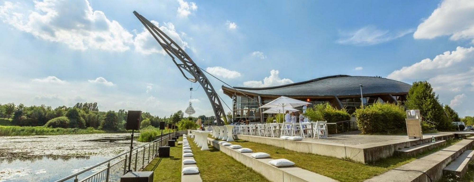 Außenansicht des Expowals auf dem Messegelände Hannover mit markant geschwungener Dachform, schrägem Turm, Grünflächen und Wasseranlagen.