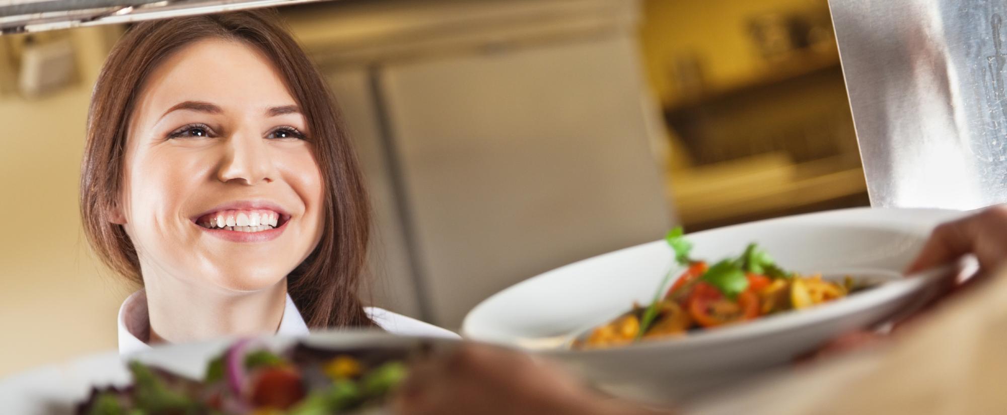 Frau lächelt beim Servieren eines Tellers mit Fleisch und Beilage in einem Restaurant.
