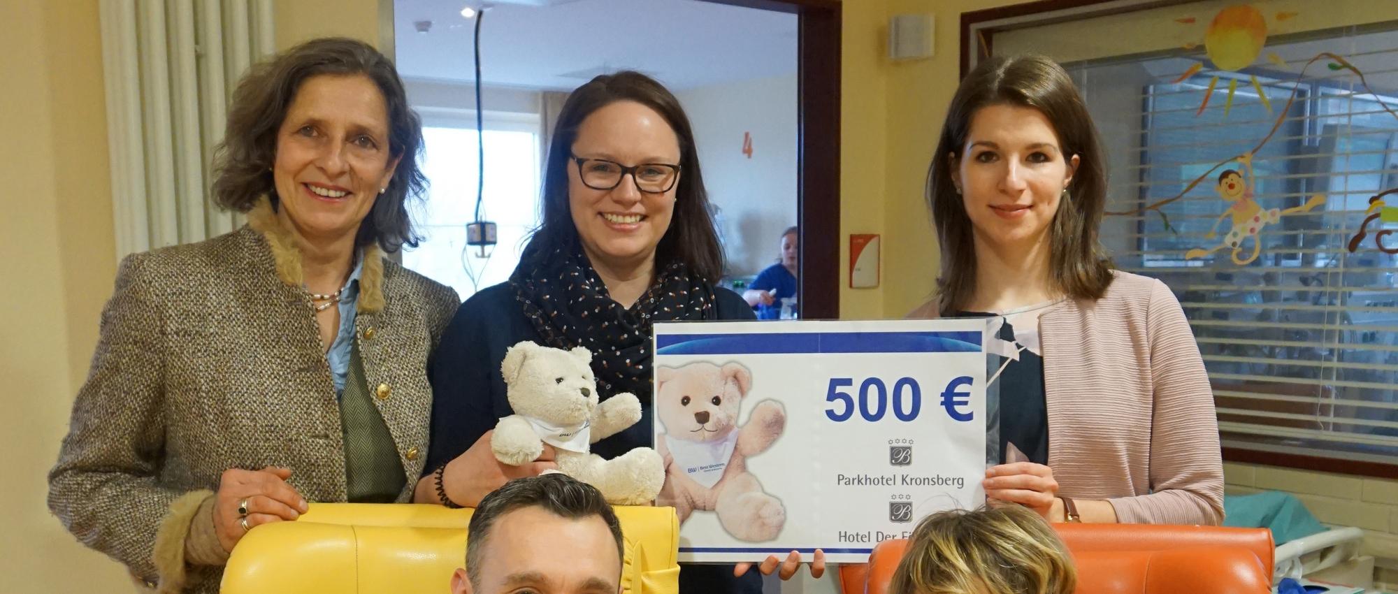 Drei Personen halten gemeinsam einen großen Spendenscheck und lächeln in die Kamera.