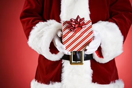 Weihnachtsmann in rotem Kostüm hält eine rot-weiß gestreifte Geschenkbox vor rotem Hintergrund