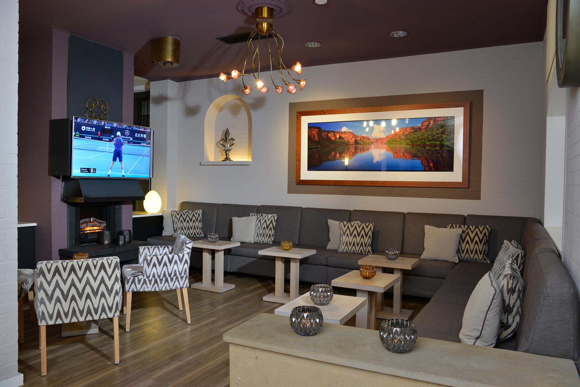 Modernes Kaminzimmer mit Holzfußboden, gemütlichen Sitzgruppen, Wand-TV, Kunstwerken und warmem Licht durch Pendelleuchten.