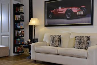 Gemütliche Wohnecke mit weißem Sofa, gemusterten Kissen, schwarzer Stehlampe und Bücherregal vor hellen Wänden und Holzfußboden.