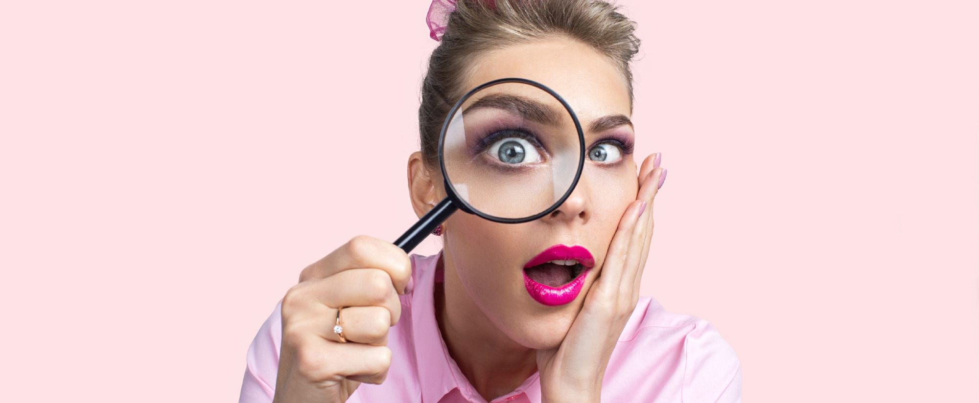 Person mit verschwommenem Gesicht, pinkem Shirt und Haaraccessoire, hält Lupe vor rosa Hintergrund.