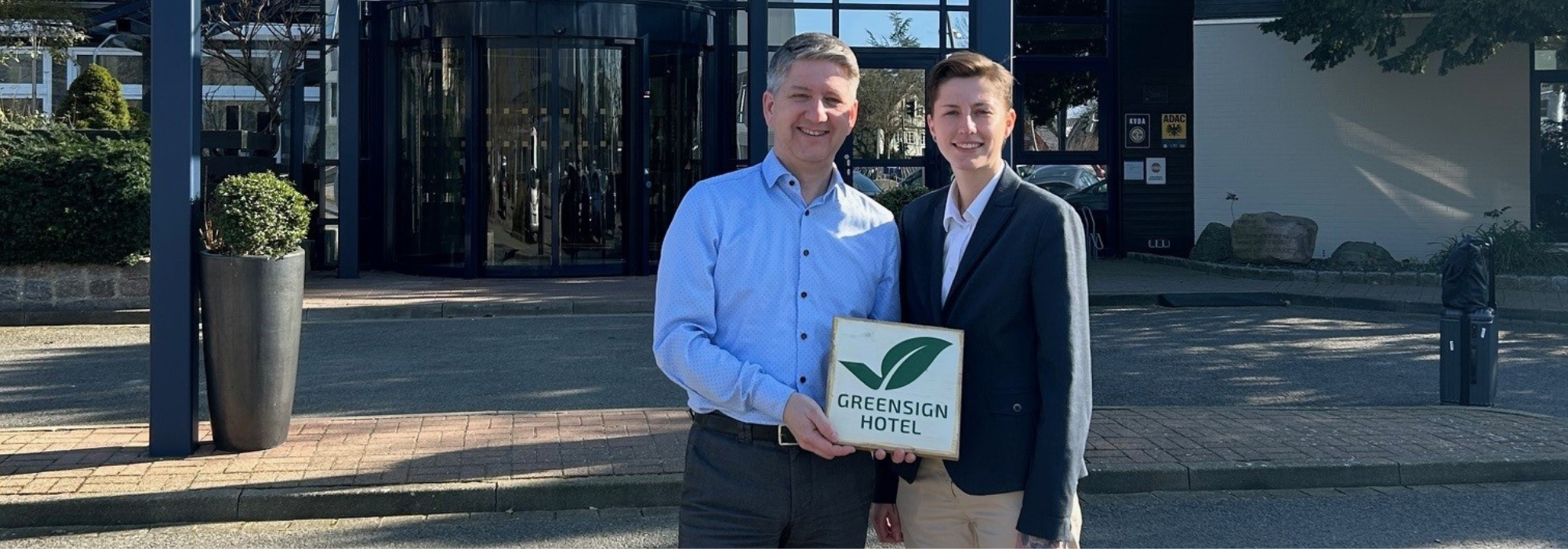 Andreas Triebsch und Viktoria Zschommler vor dem Hotel, mit einer gerahmten GreenSign Urkunde in den Händen.