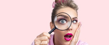 Person mit verschwommenem Gesicht, pinkem Shirt und Haaraccessoire, hält Lupe vor rosa Hintergrund.