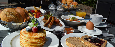 Frühstückstisch im Freien mit Gebäck, Brot, Obst, Ei, Orangensaft und Kaffee – Terrassenambiente.