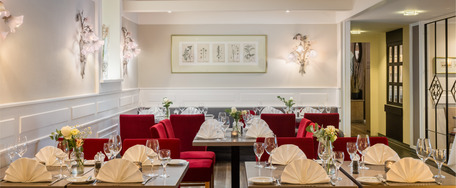 Luxuriöser Speiseraum mit langem, weiß gedecktem Tisch, roten Polsterstühlen, Wandverzierungen und warmem Licht.