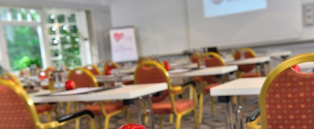 Tagungsraum mit Tischreihen, roten Stühlen, Notizmaterial und Äpfeln auf jedem Platz.